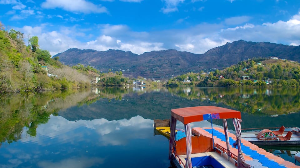 A calm lake with a boat docked on the right, surrounded by lush greenery and mountains in the background.