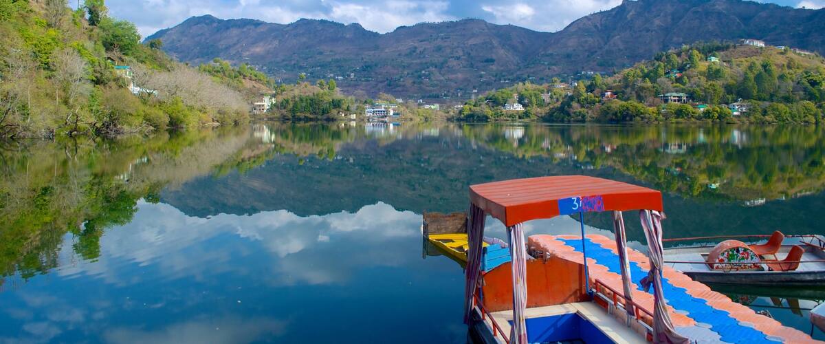 A calm lake with a boat docked on the right, surrounded by lush greenery and mountains in the background.