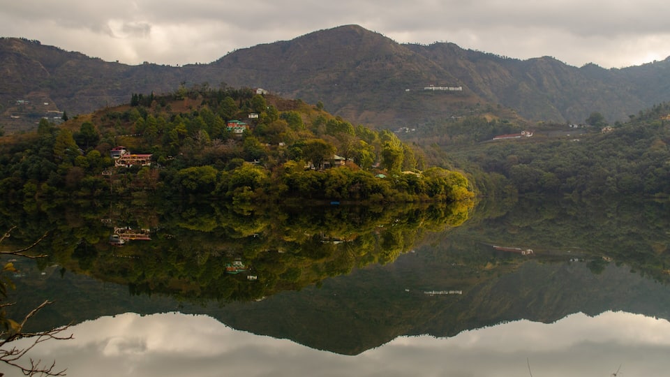 A serene lake with a reflection of the surrounding hills and a few buildings.