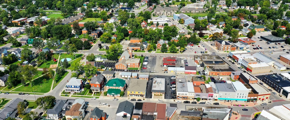An aerial view of a town with a mix of residential and commercial buildings, roads, and green spaces.