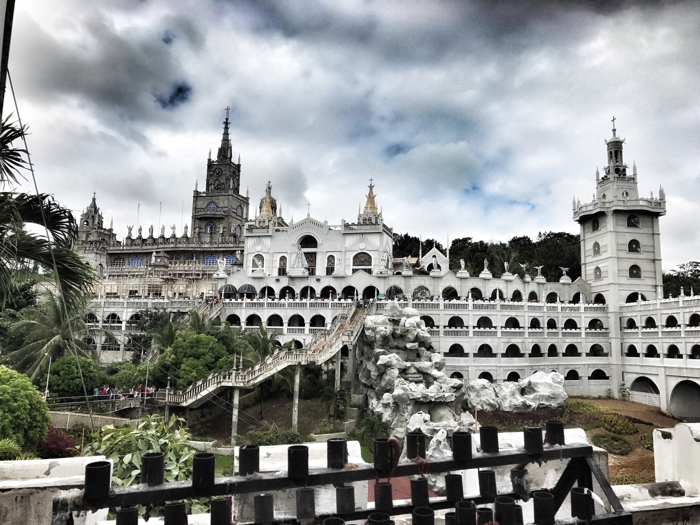 A grand, ornate building with multiple towers and statues, surrounded by lush greenery.