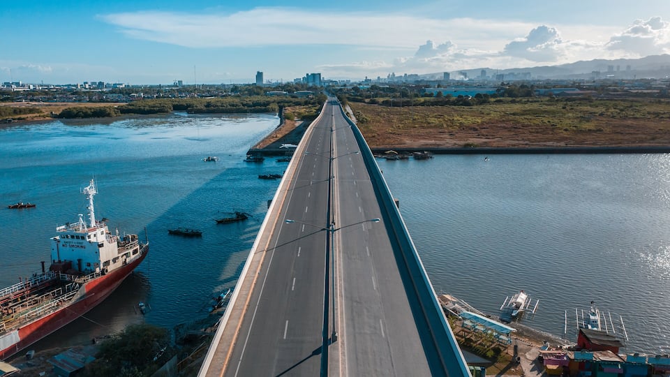 A long bridge over a river with boats and a cityscape in the background.