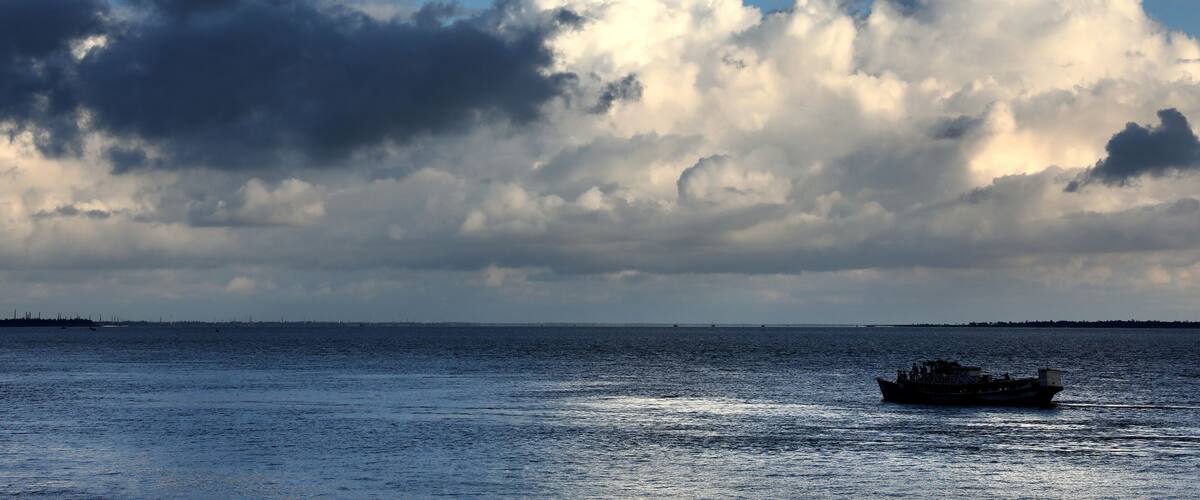A boat on a calm sea with a dramatic sky filled with clouds.