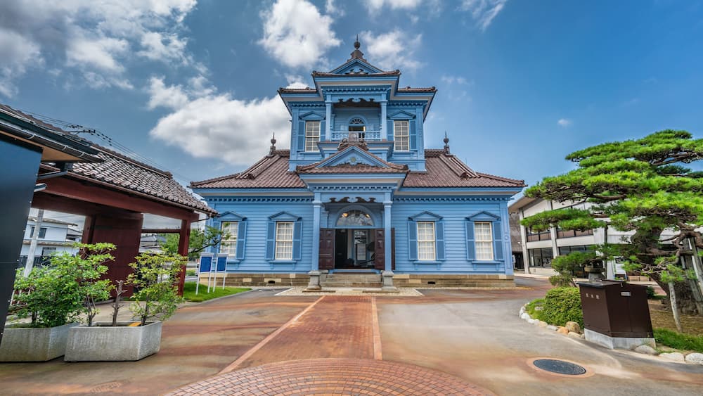 A traditional blue building with a tiled roof, surrounded by a paved walkway and greenery.