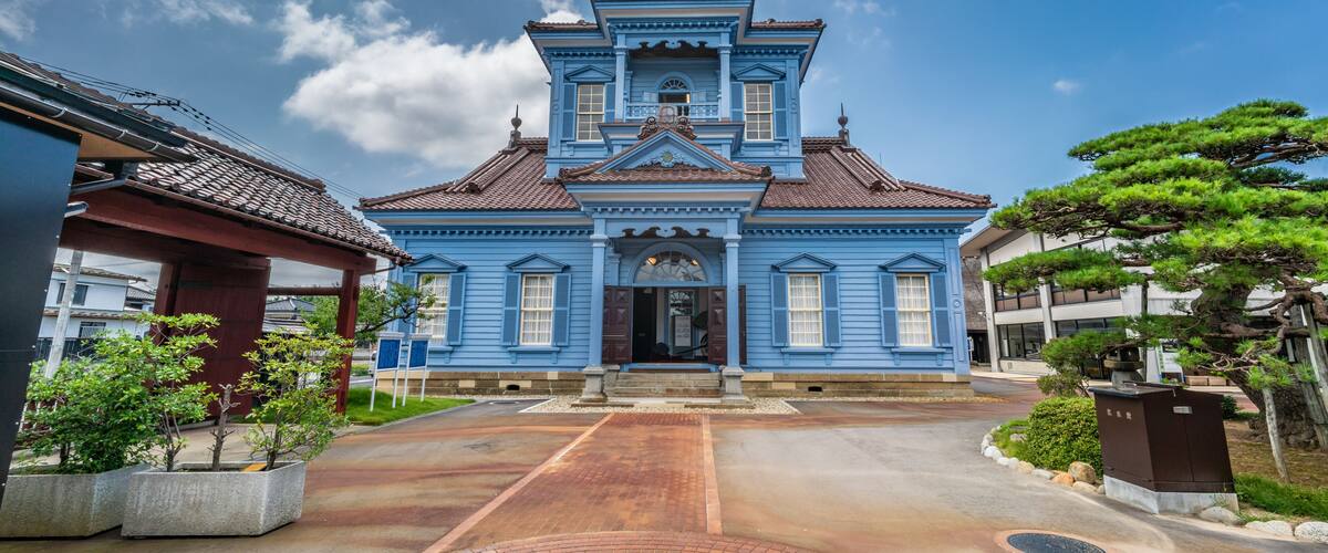 A traditional blue building with a tiled roof, surrounded by a paved walkway and greenery.