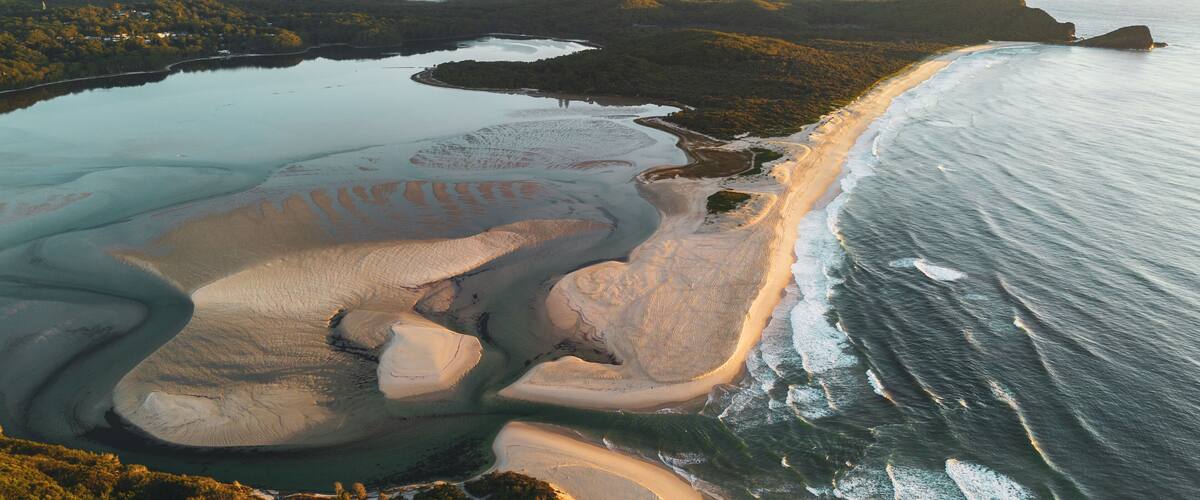 Un paysage côtier avec une plage de sable, des eaux calmes et des collines environnantes.