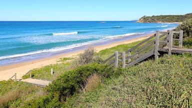 A beach with a wooden staircase leading down to the shore, surrounded by greenery.