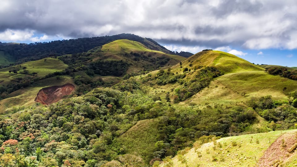 Rolling hills, dense greenery, and a prominent red rock formation.