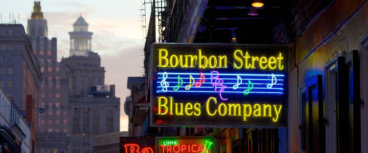Colorful neon signs illuminate Bourbon Street's vibrant nightlife in New Orleans during twilight hours
