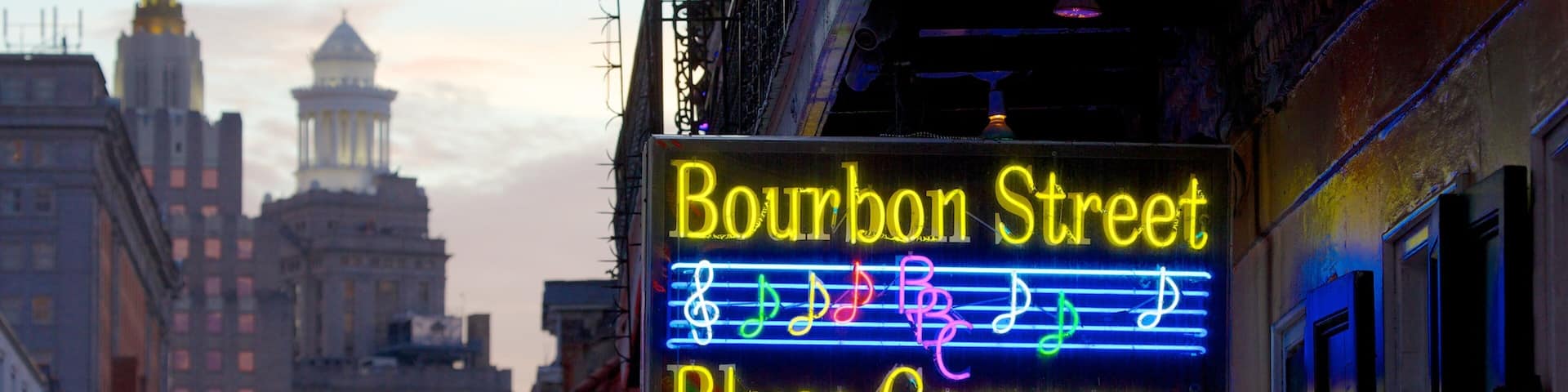 Colorful neon signs illuminate Bourbon Street's vibrant nightlife in New Orleans during twilight hours