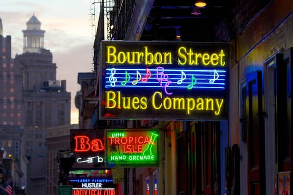 Colorful neon signs illuminate Bourbon Street's vibrant nightlife in New Orleans during twilight hours