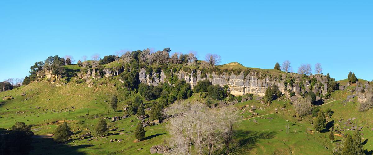 A green hillside with a rocky cliff and a building on top.