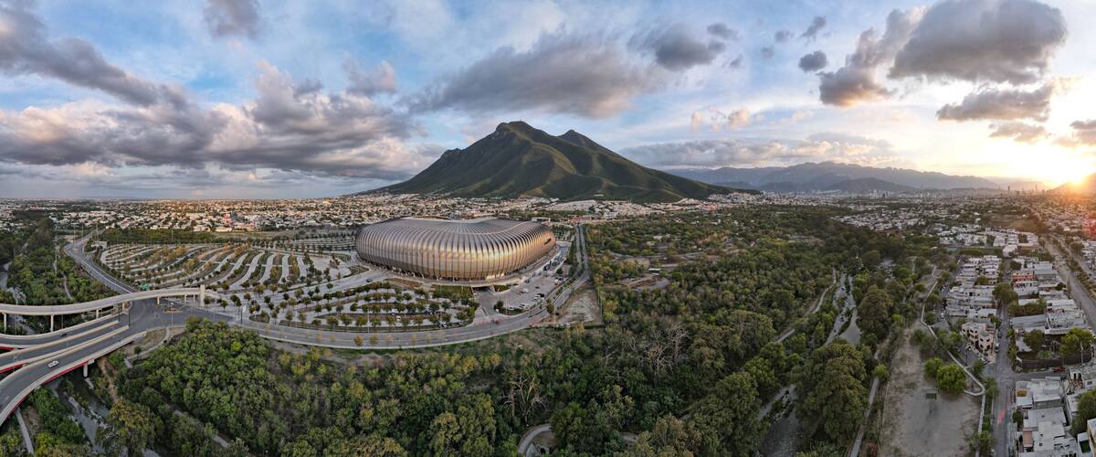 A stadium surrounded by a park, a mountain, and a cityscape.