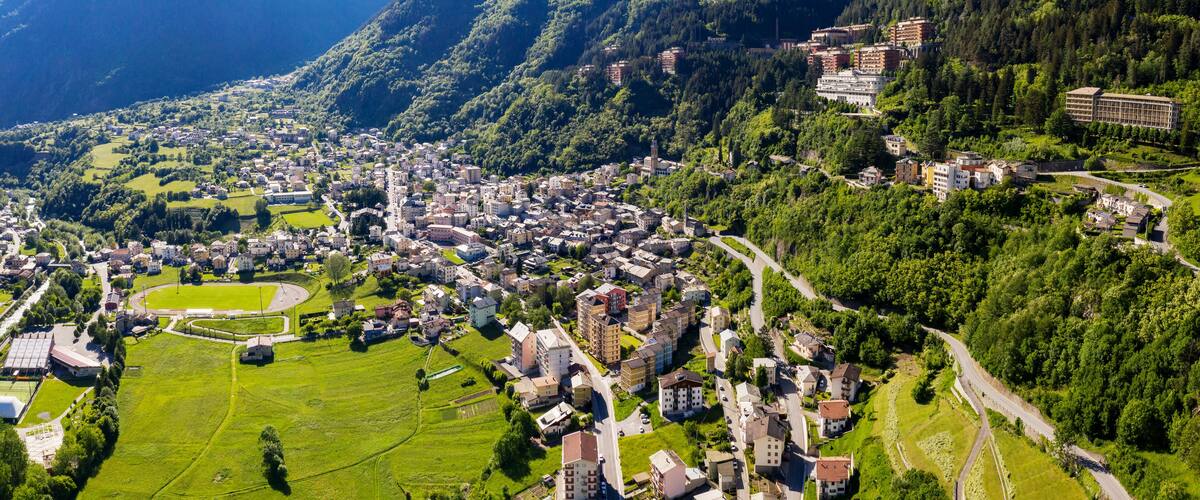 A mountainous town with dense greenery, a central open field, and buildings clustered along the hillside.