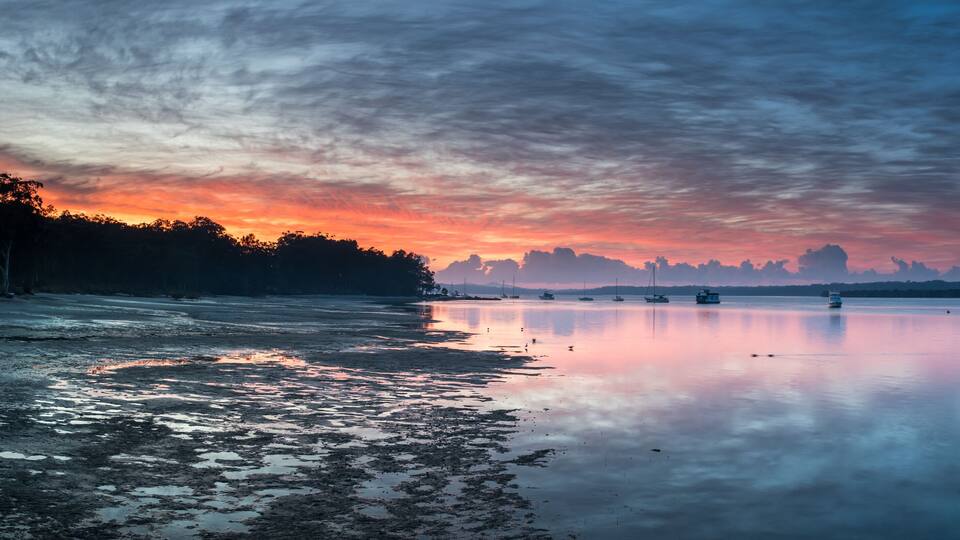 Un lago tranquilo al atardecer, con barcos y una orilla cubierta de bosque.