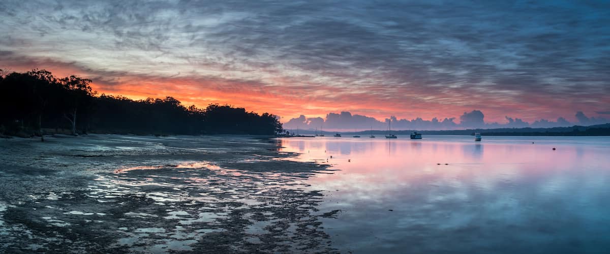 A calm lake at sunset with boats and a forested shoreline.