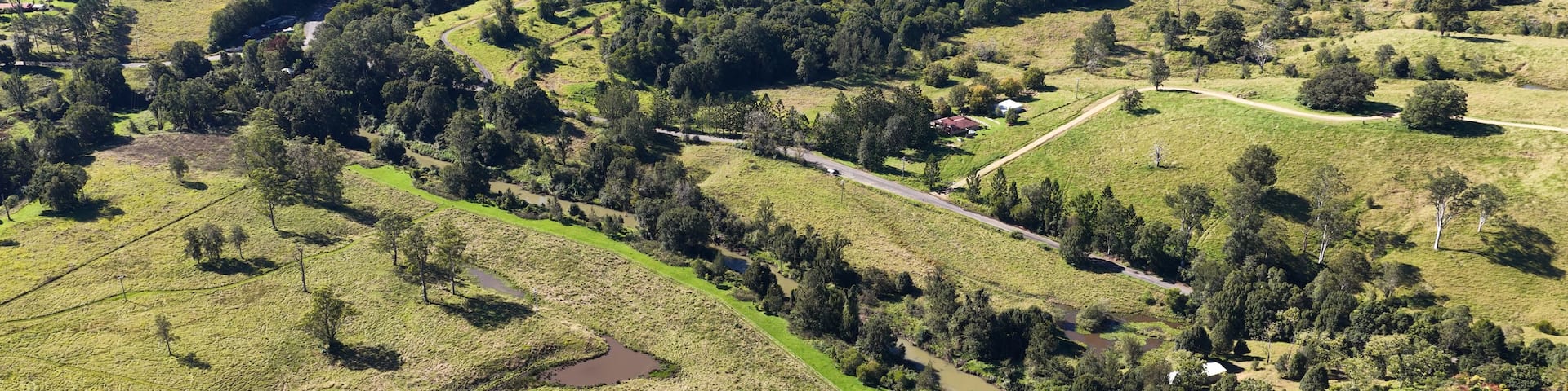 A rural landscape with rolling hills, a winding road, and scattered buildings.