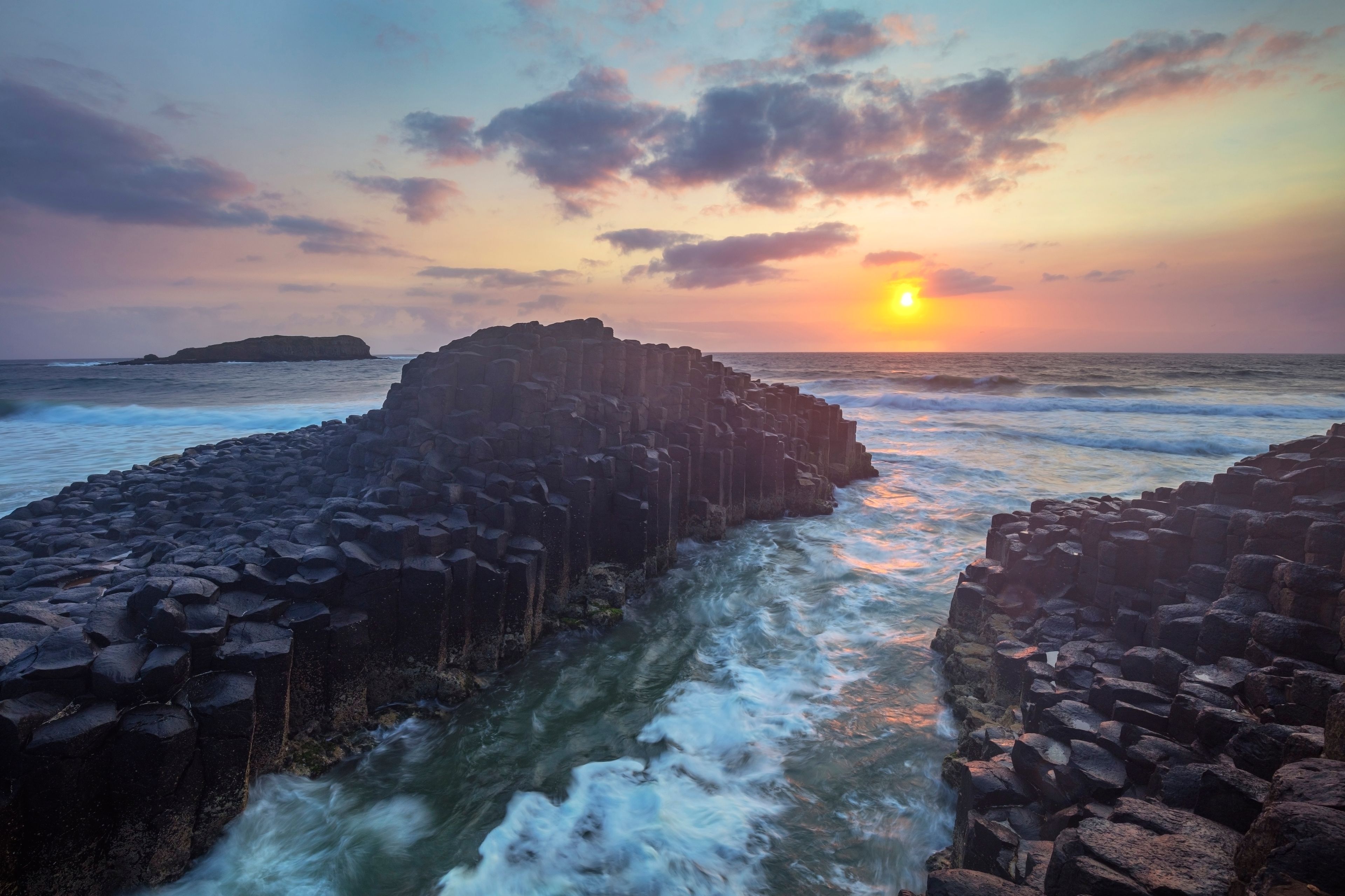 A rocky coastline at sunset with waves crashing against the rocks.
