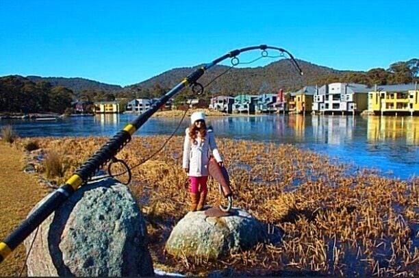 A person fishing by a river with houses in the background.