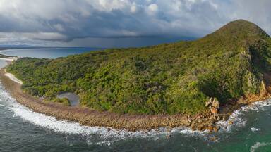 Panoramic aerial view of a rainbow over a coastal headland with dramatic clouds above