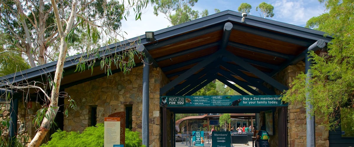 A zoo entrance with a stone building, green signage, and a covered walkway.