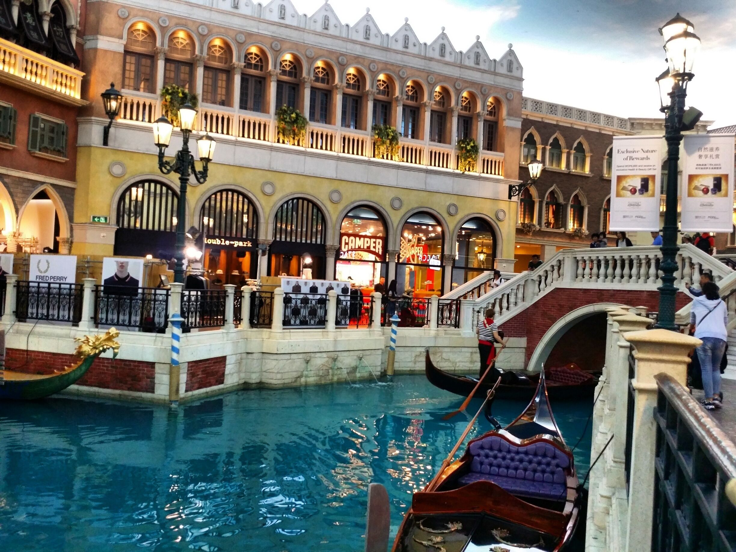 A canal with gondolas, a bridge, and Venetian-style buildings with shops.