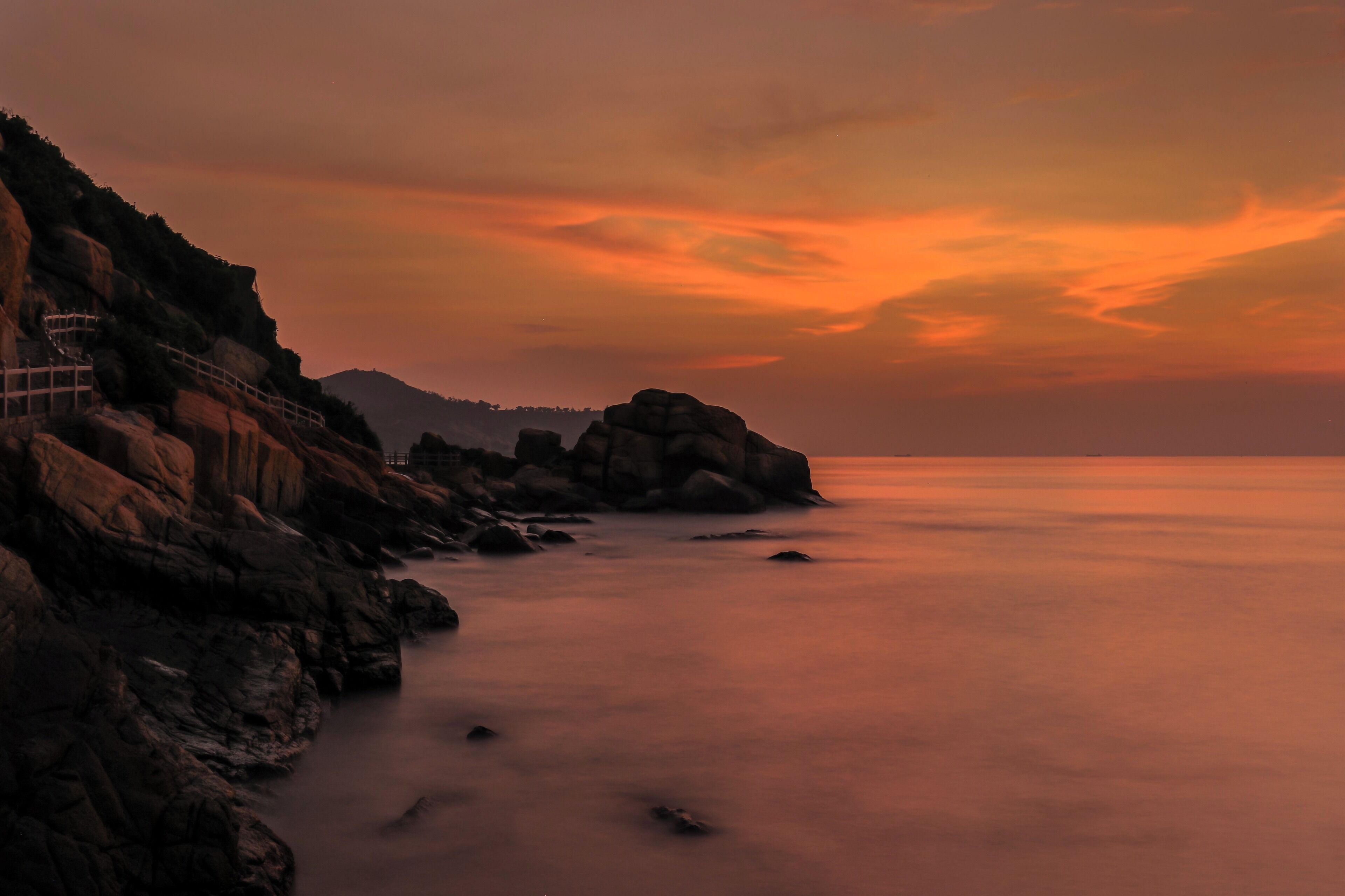 A coastal landscape with rocky cliffs and a calm sea at sunset.