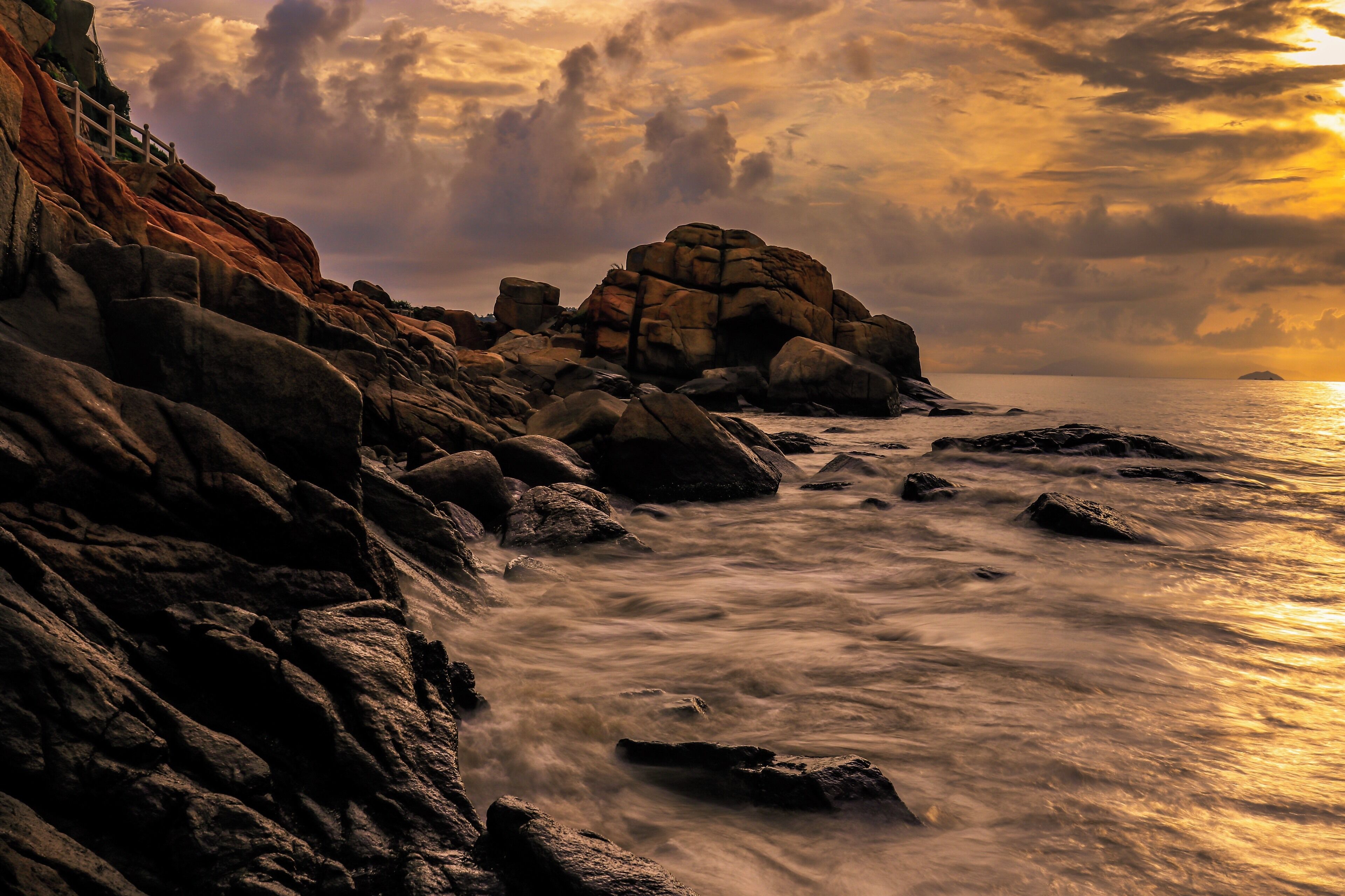 A rocky coastline with a wooden fence and a large rock formation.