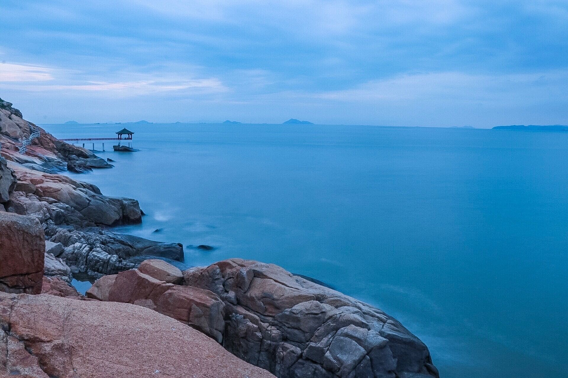 Una costa rocosa con un muelle que se adentra en aguas azules y tranquilas.