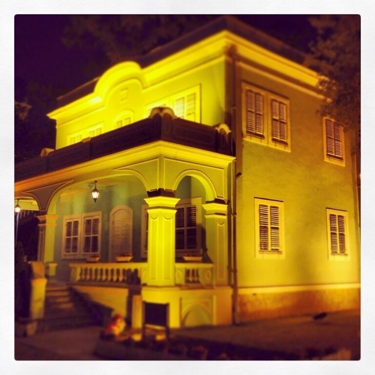 A two-story building with a balcony and arched windows, illuminated by yellow lights.