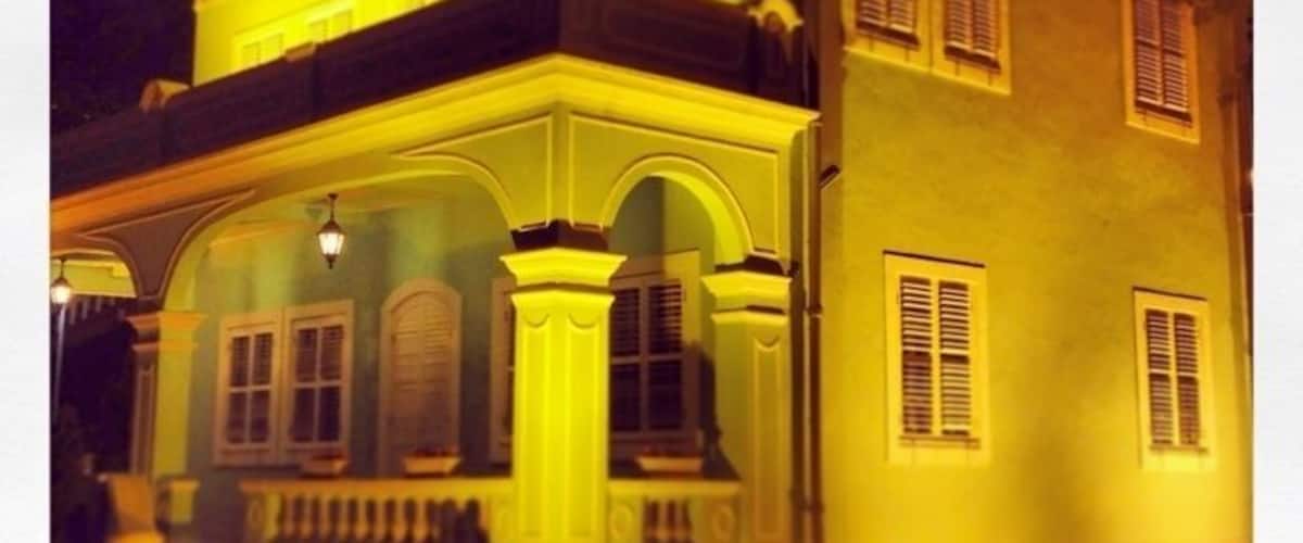 A two-story building with a balcony and arched windows, illuminated by yellow lights.