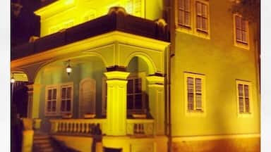 Um edifício de dois andares com varanda e janelas em arco, iluminado por luzes amarelas.