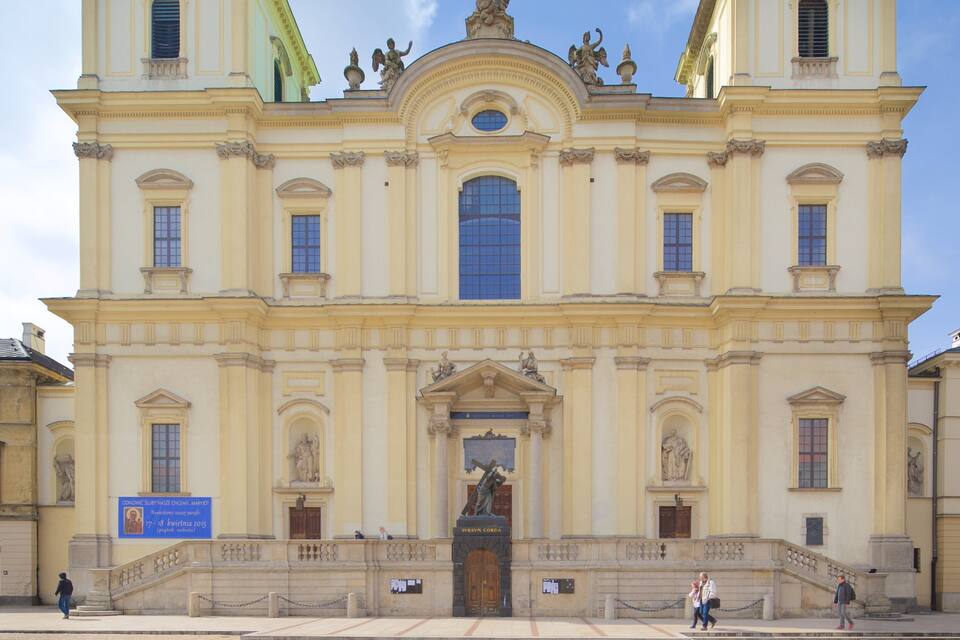 Un edificio grande y ornamentado con una entrada central, estatuas y un ventanal azul.