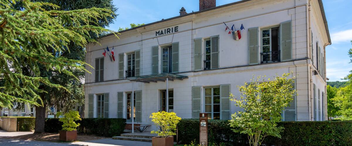 A two-story building named MAIRIE with green shutters, a brick chimney, and a small balcony.