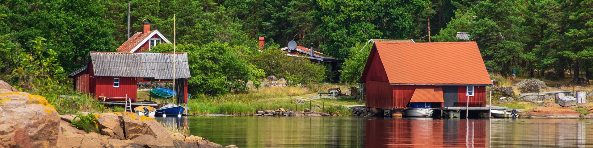 A calm lake with red buildings on stilts, surrounded by dense green forest.
