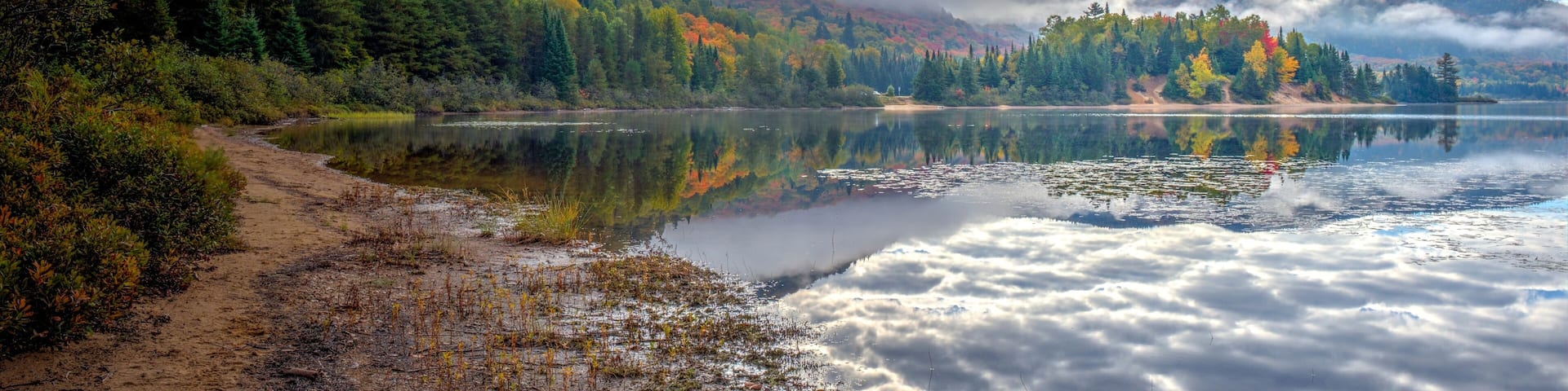 A lake surrounded by forested mountains, with a trail leading to the water's edge.