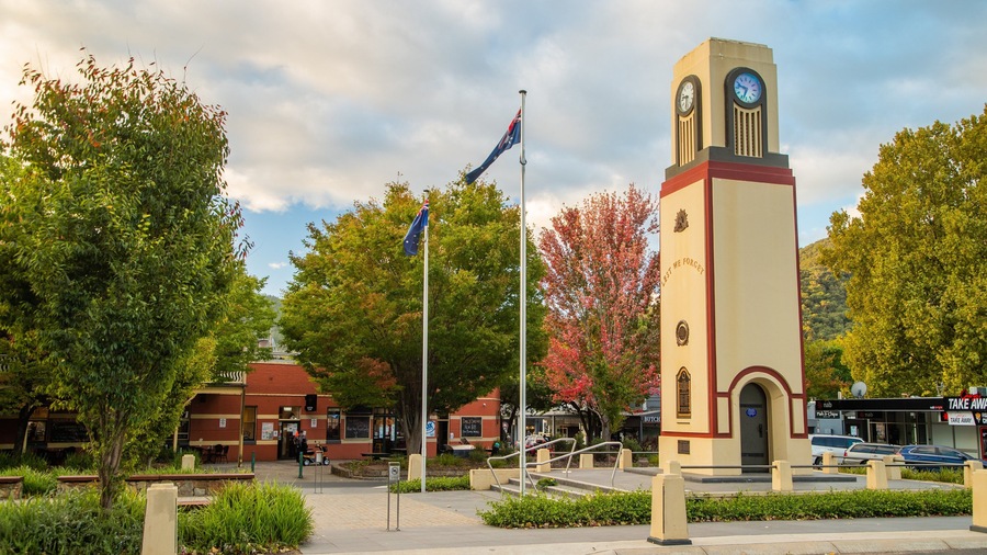 A clock tower with a plaque reading "LAST WE FORGET" surrounded by trees and a flagpole with flags.