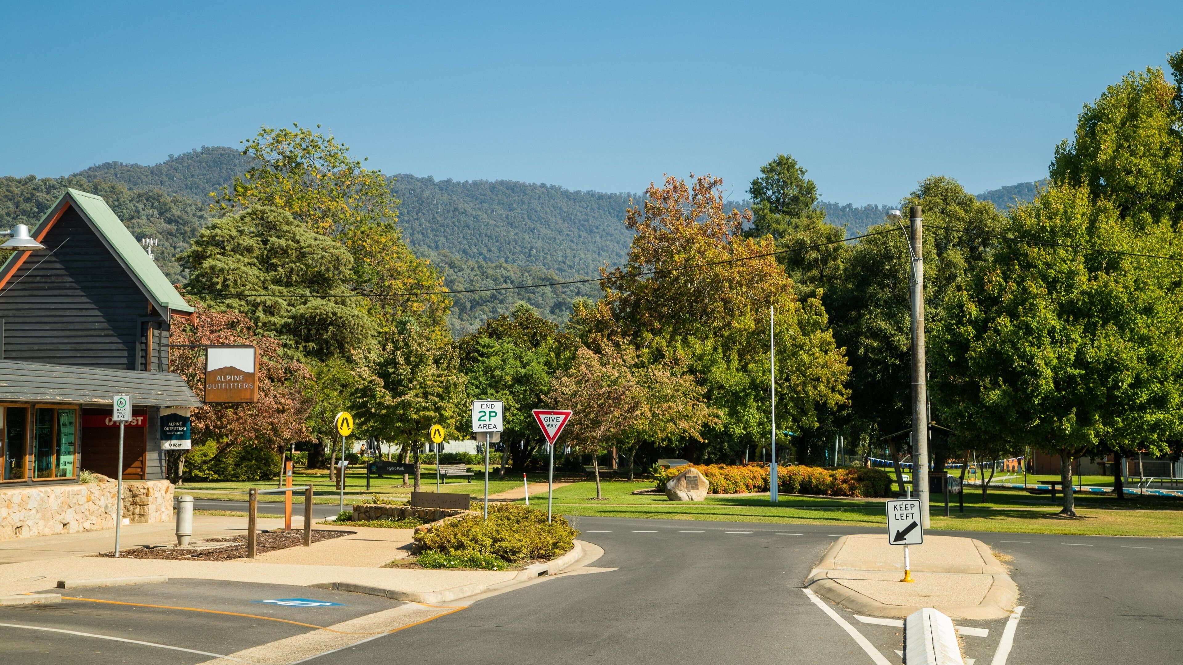 A street intersection with a mountain in the background, a building labeled 'Alpine Outfitters', and road signs including 'End 2nd Ave' and 'Give Way'.