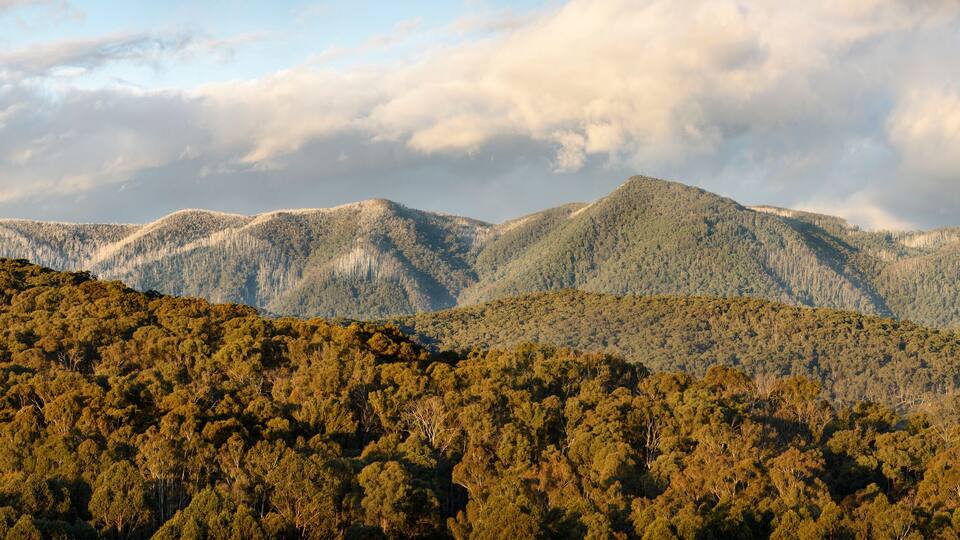A mountainous landscape with dense forested hills and a cloudy sky.