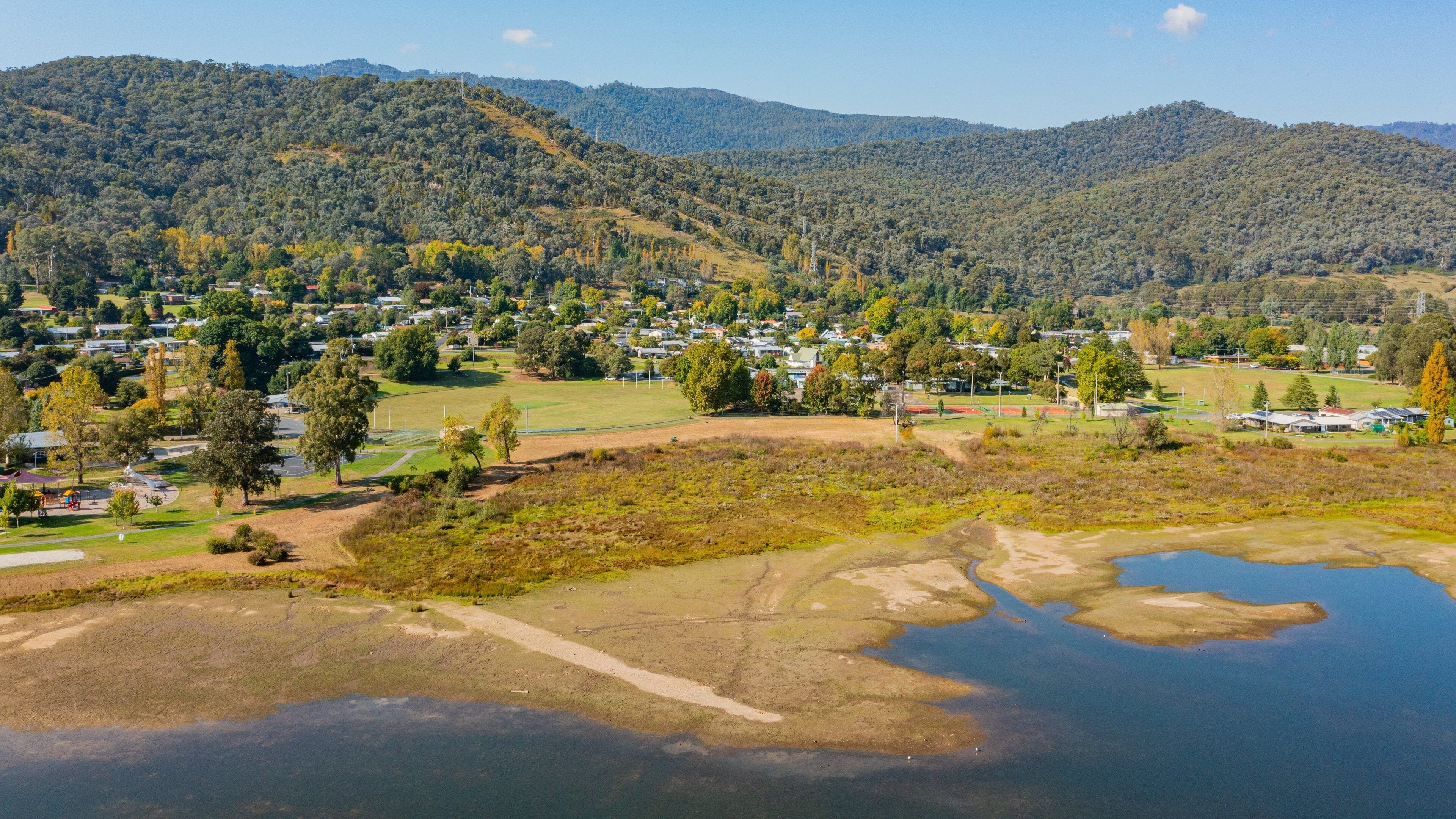 A lakeside town with houses, a park, and forested hills.