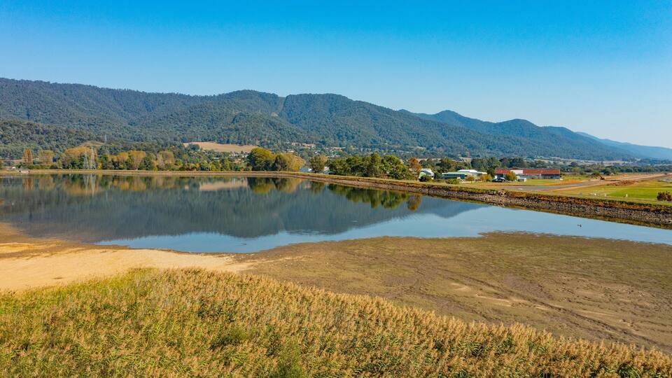 A lake with a reflection of the surrounding landscape, including mountains and buildings.