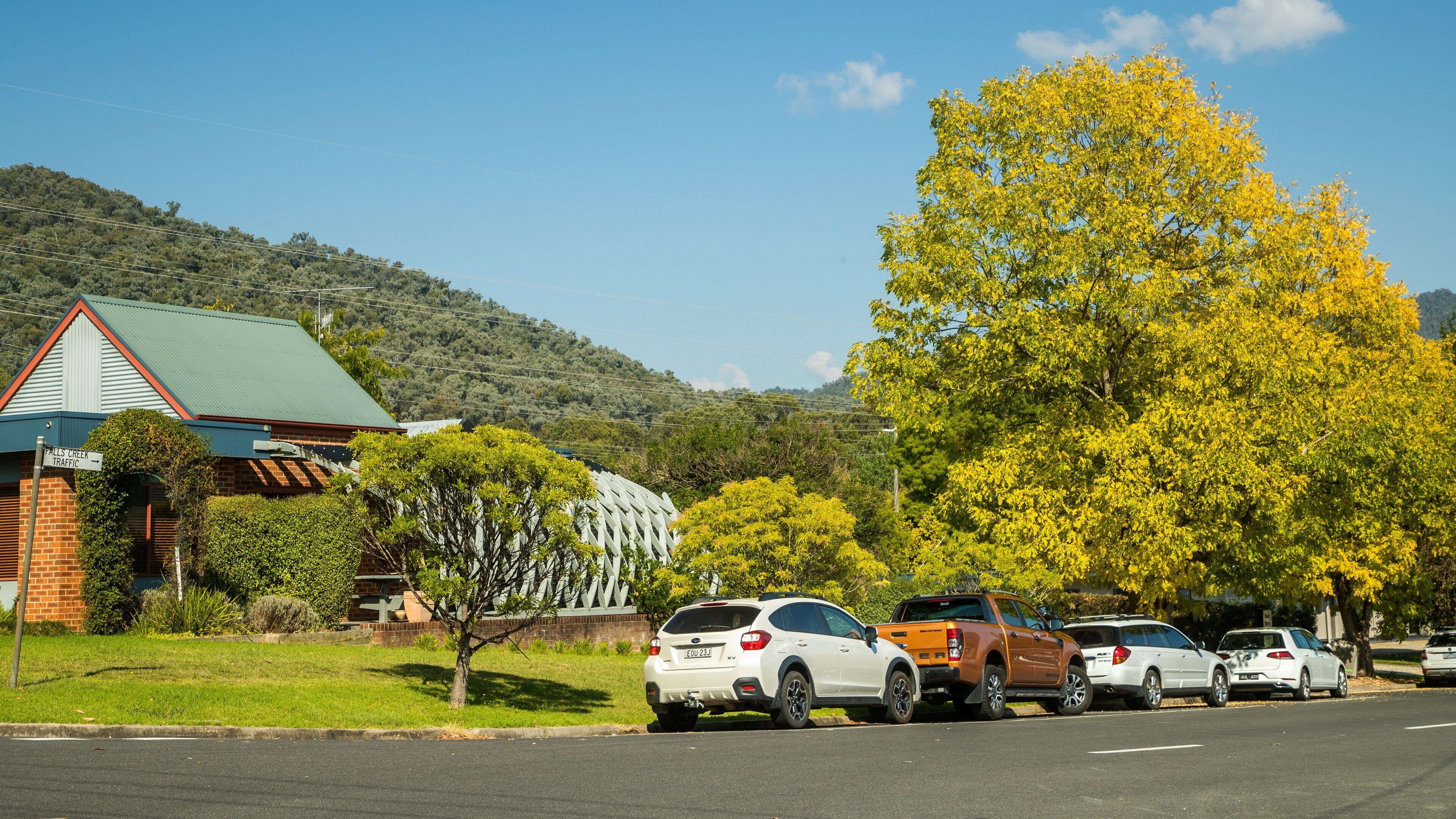 A parking lot with cars, a building with a green roof, and a hill with trees in the background.