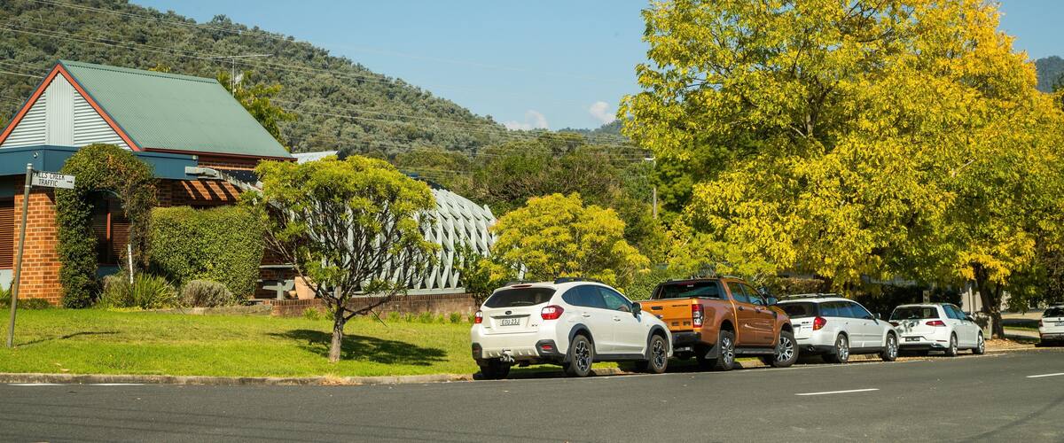 A parking lot with cars, a building with a green roof, and a hill with trees in the background.