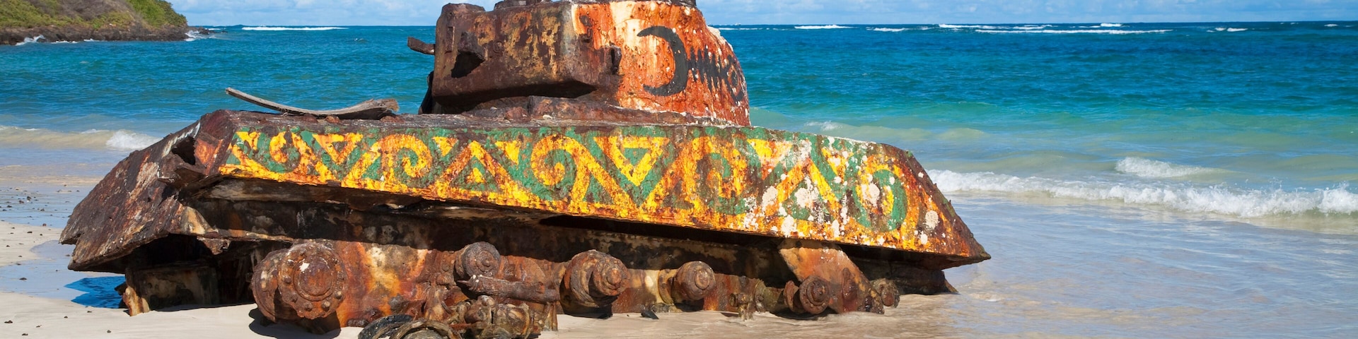 A rusted tank with colorful paint on a beach.