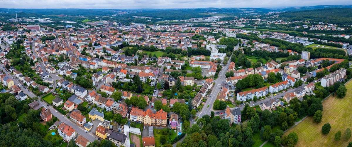 An aerial view of a densely populated town with red-roofed houses, green spaces, and a prominent church.