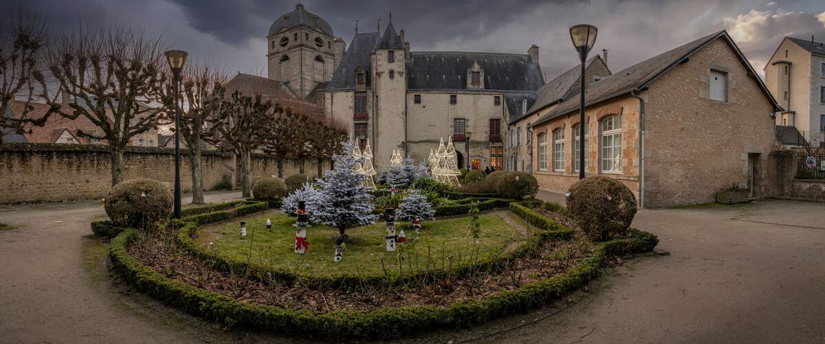 A historic building with a tower, surrounded by a well-maintained garden with snow-covered trees and a paved path.