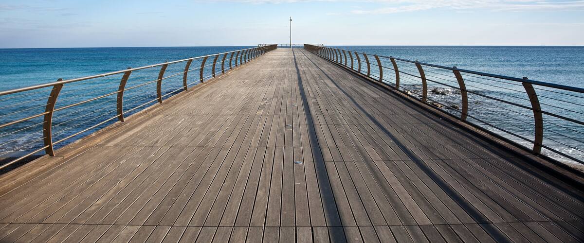 A wooden pier extending into the sea with railings on both sides.