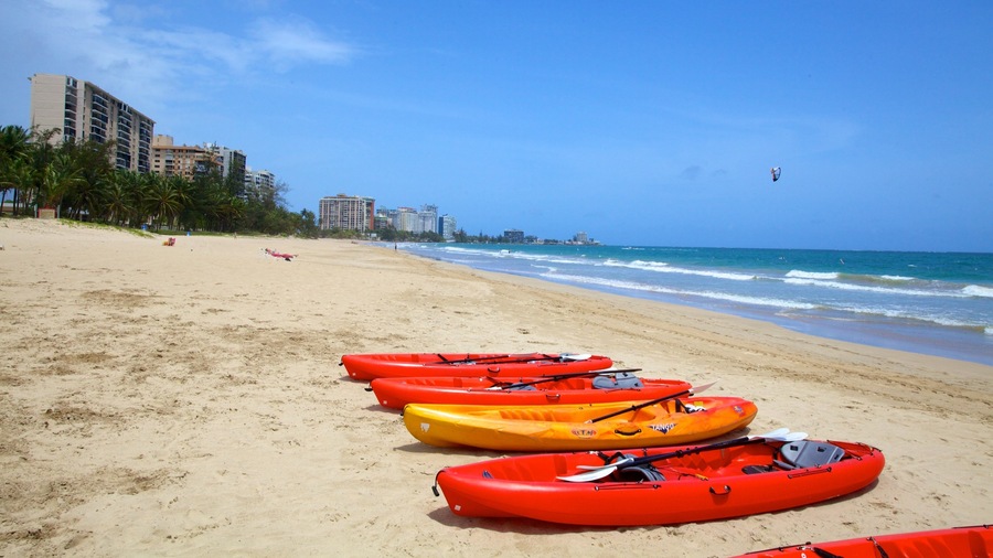 A beach with kayaks lined up on the sand and a kite surfer in the air.