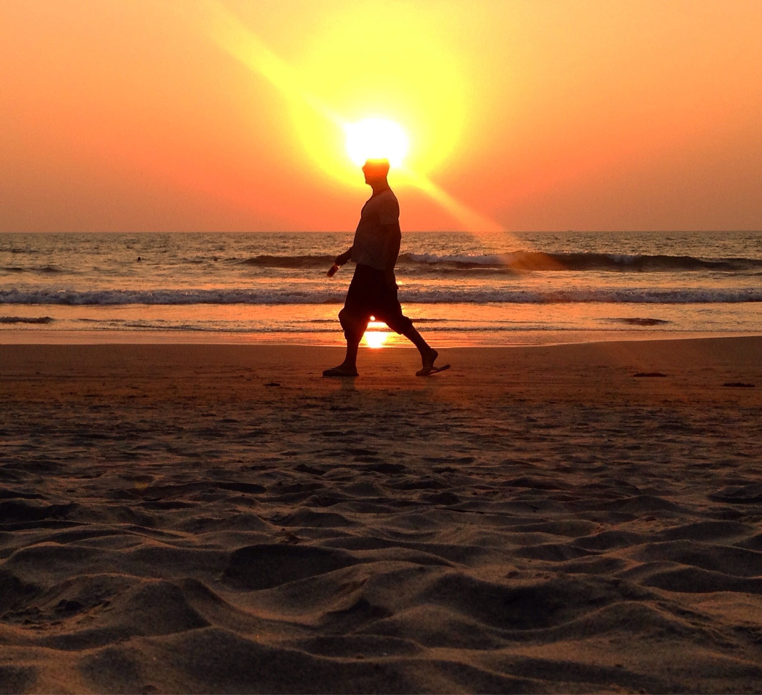 A person walking on a beach at sunset.