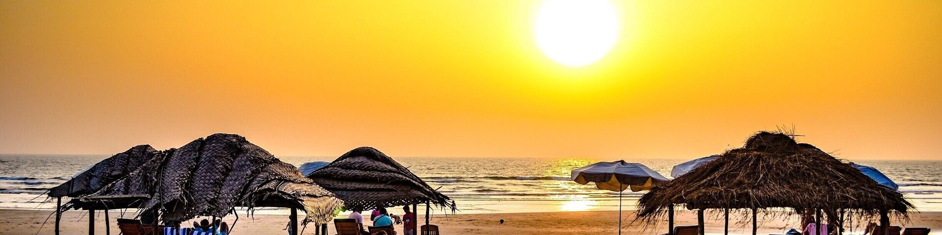 Una playa con sombrillas de paja y sillas de madera para tomar el sol al atardecer.